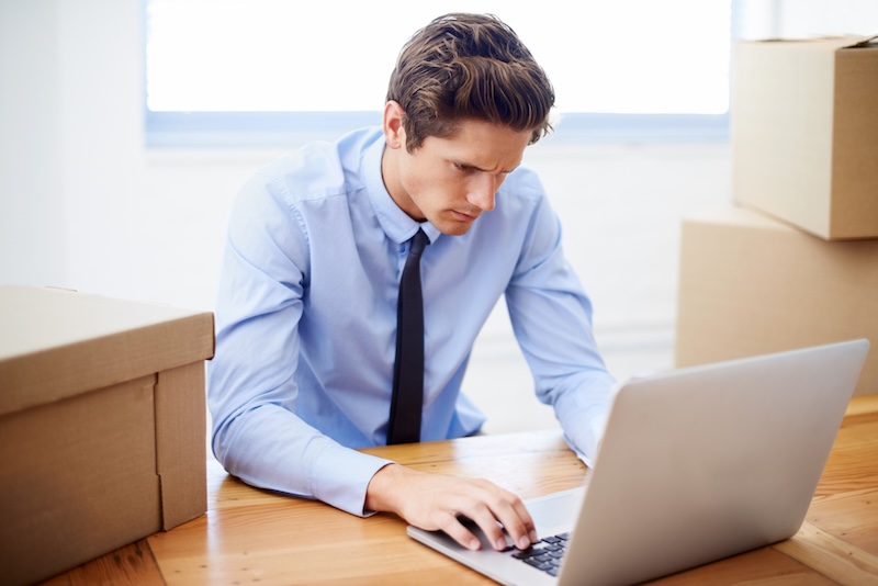 Man på kontor vid laptop med flyttlådor runt
